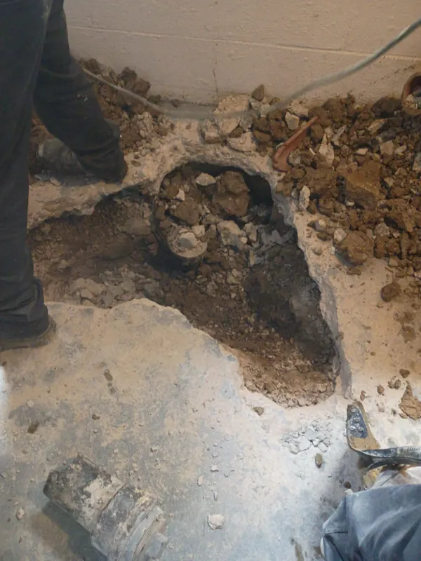 An open floor cut beside a wall where a water service enters a commercial building