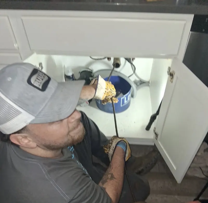 A DrainMaster technician working a drain cable under a bathroom vanity