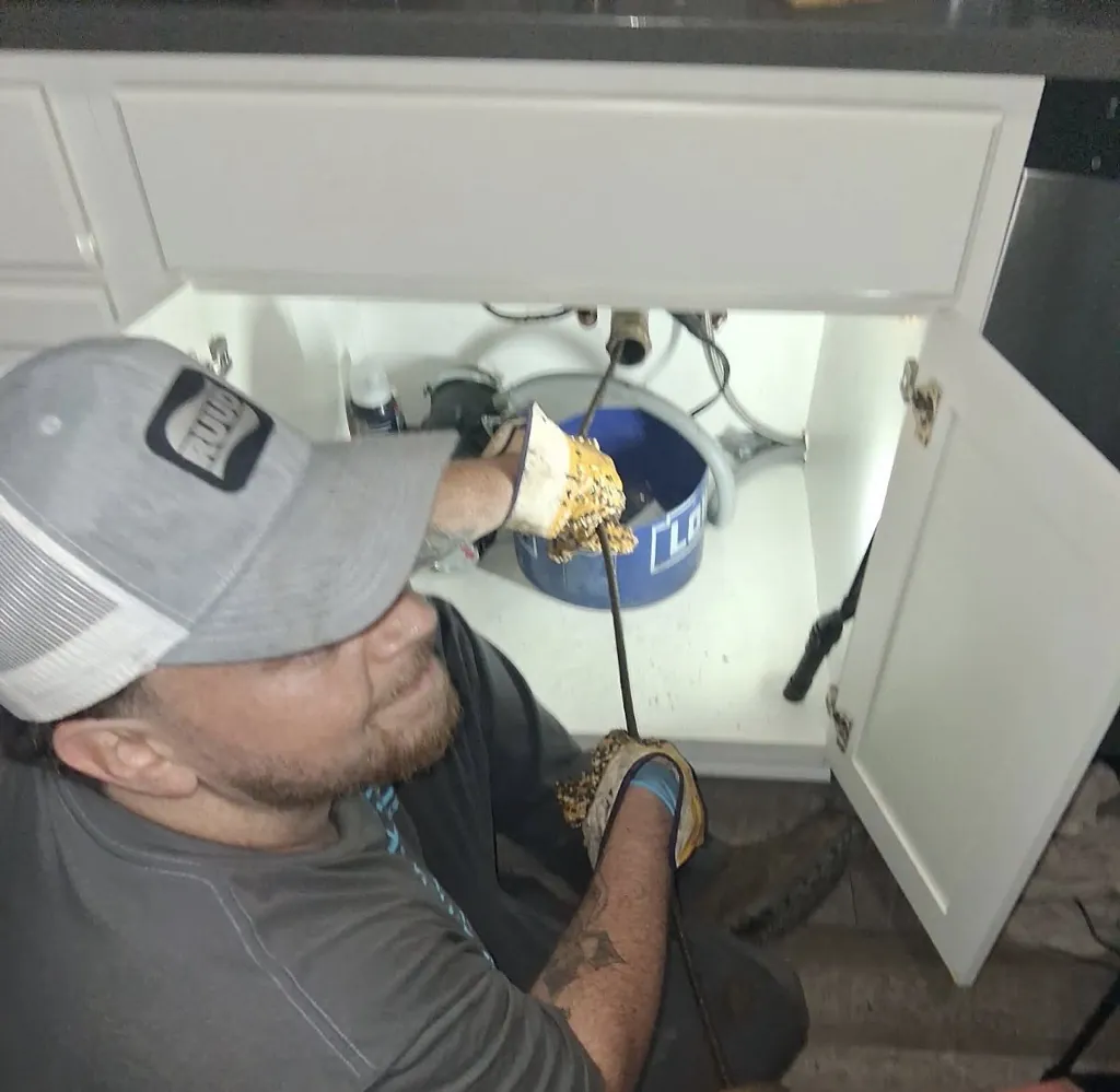 A DrainMaster technician working a drain cable under a bathroom vanity