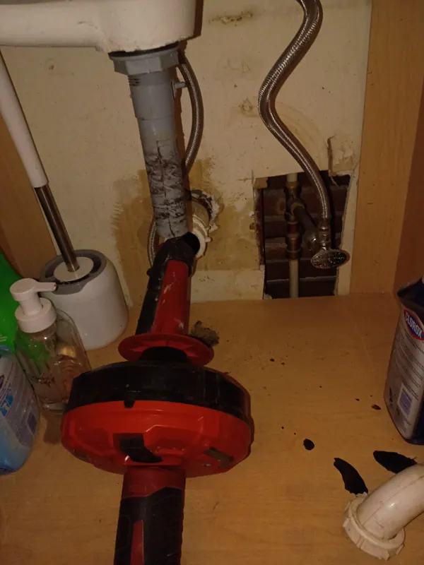 A drain machine set up beside an open vanity with the trap removed