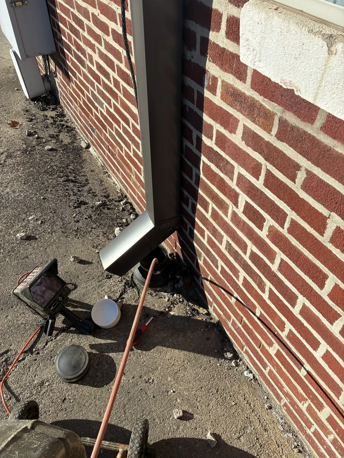Camera inspection equipment positioned against a brick wall beside an open cleanout