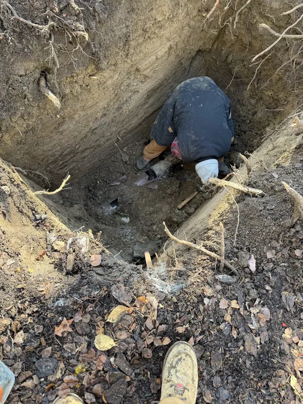 A technician working at the bottom of an open excavation over a sewer line