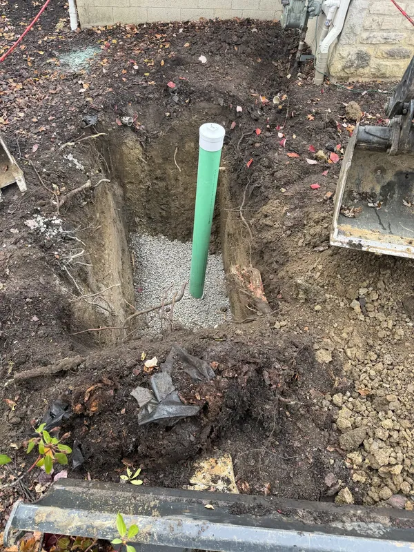 An open excavation with a new vertical cleanout riser pipe fitted to the sewer line