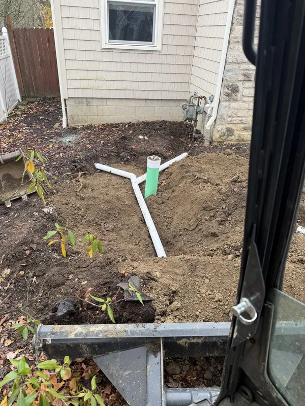 A finished white cleanout fitting standing in a yard beside a house