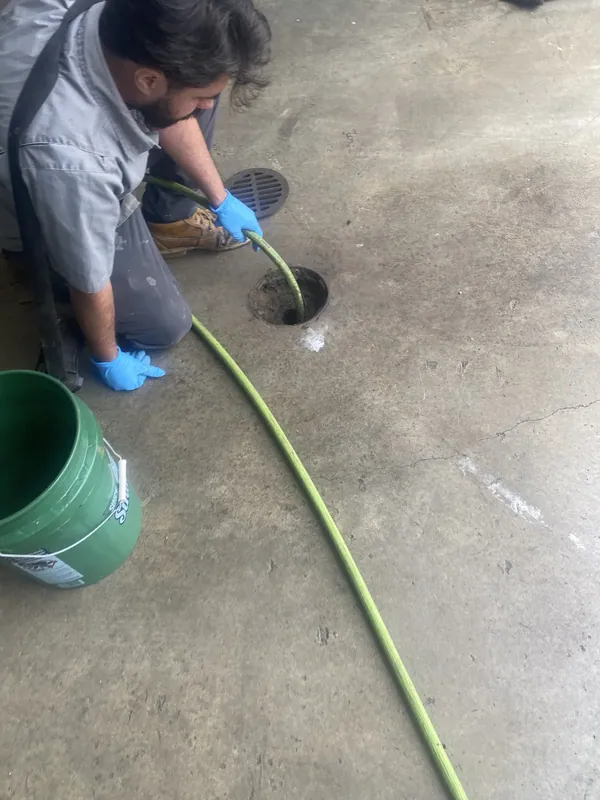 A technician in gloves feeding a jetting hose into a commercial concrete floor drain