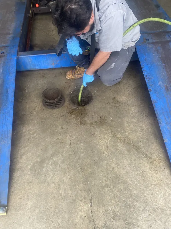 A technician working on a floor drain between racking in a commercial building