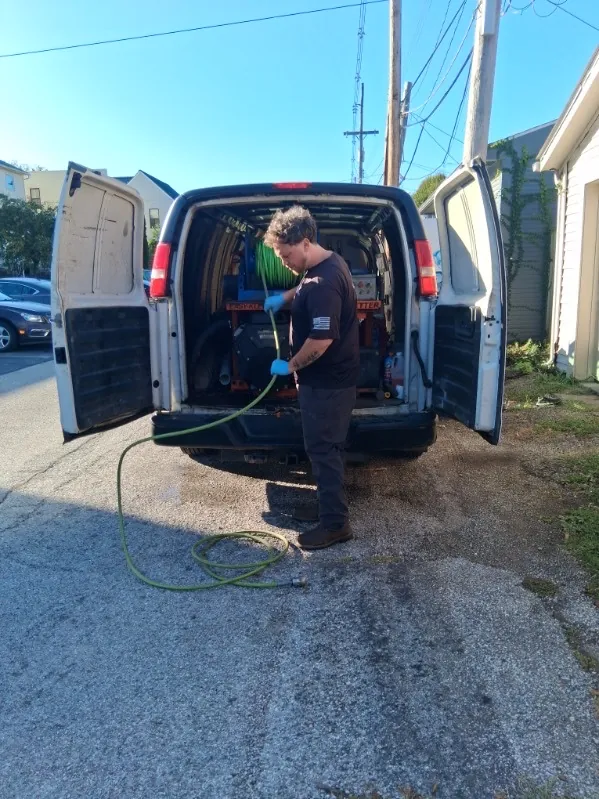 A DrainMaster technician loading a hydro-jetter at the back of a service van