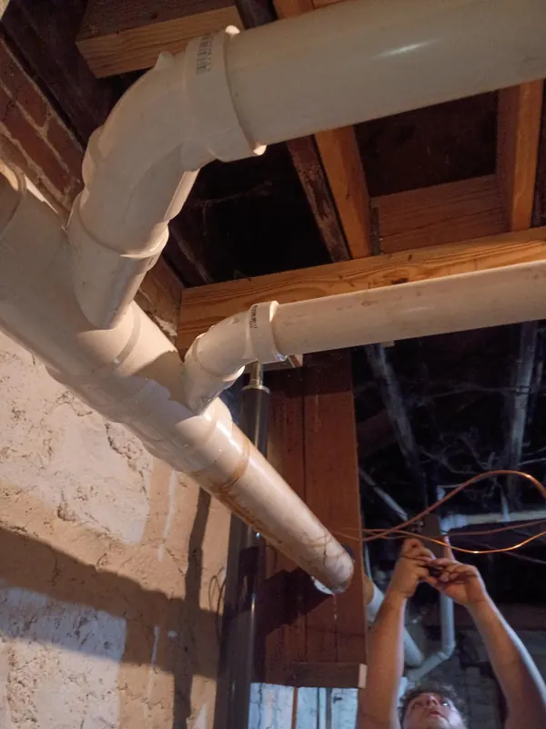 A technician fitting new PVC drain pipe overhead in an unfinished basement