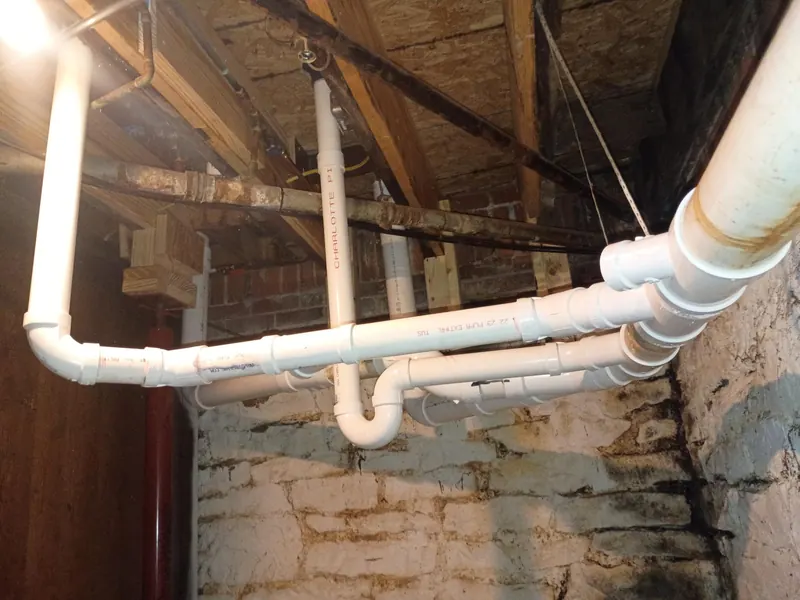 A run of new PVC drain lines and fittings suspended beneath the basement ceiling