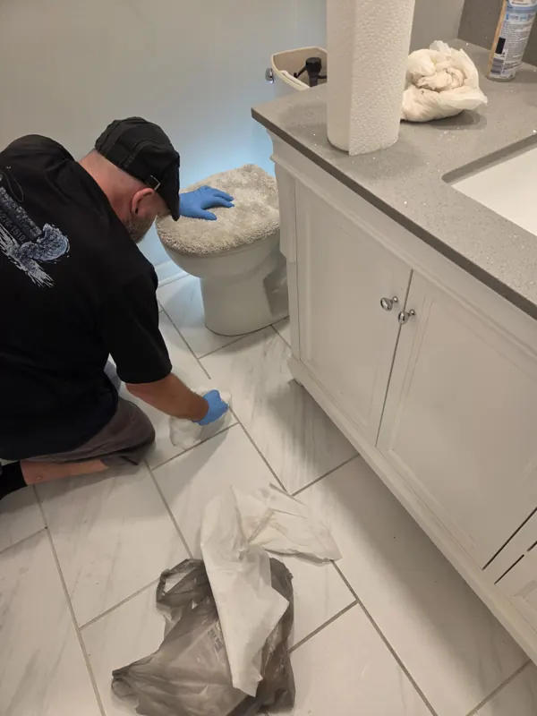 A technician kneeling to clean the floor around a toilet flange during a reset