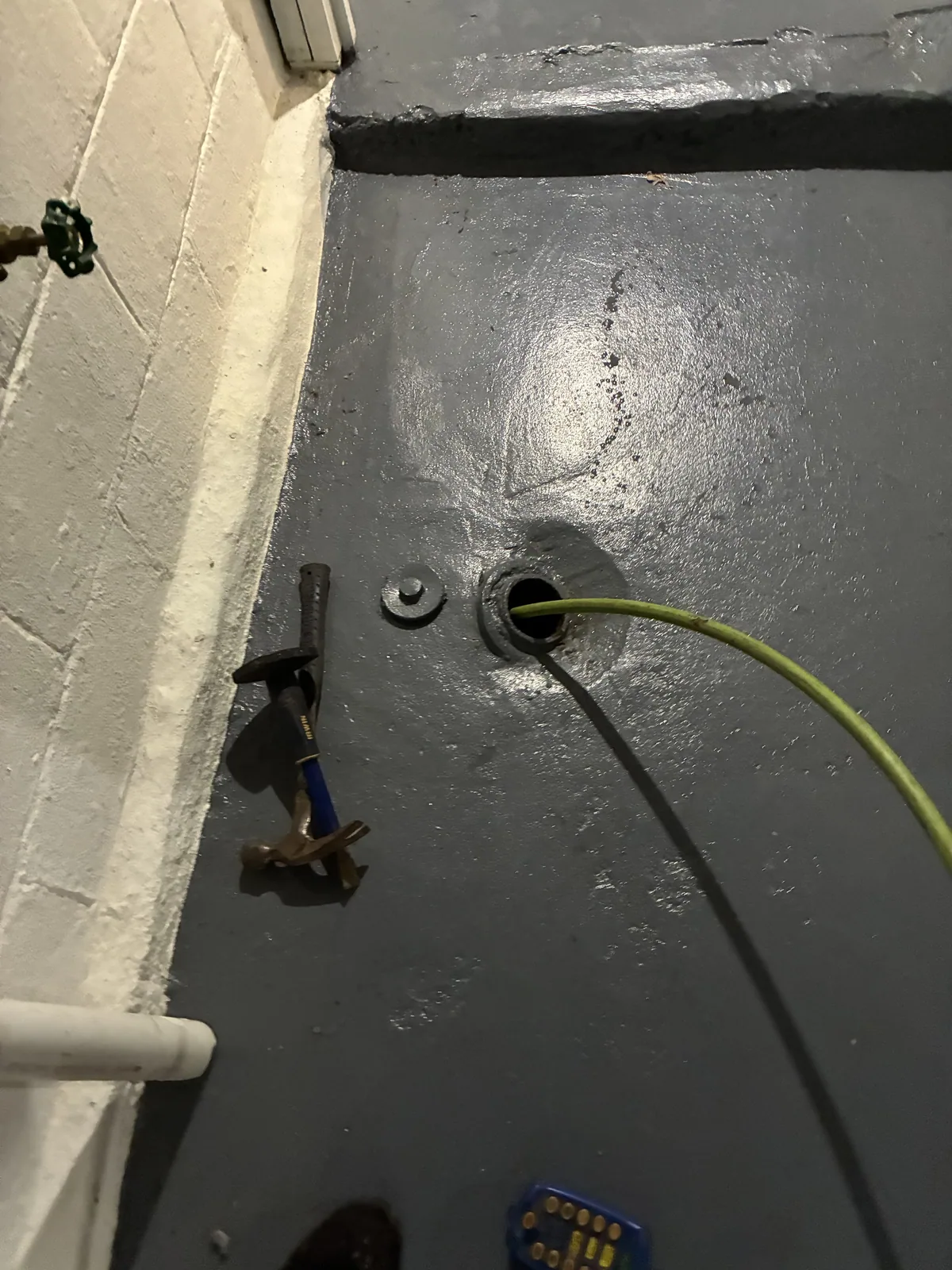 A hose run to a basement floor drain across a wet concrete floor