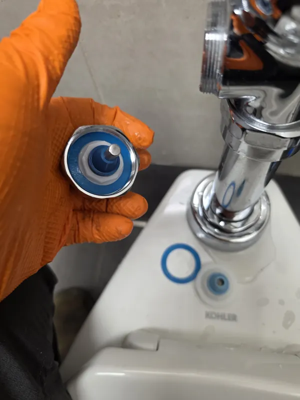 A gloved hand holding a new flush valve diaphragm kit above the fixture