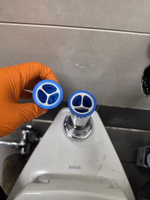 New flush valve internals held up beside the open valve body
