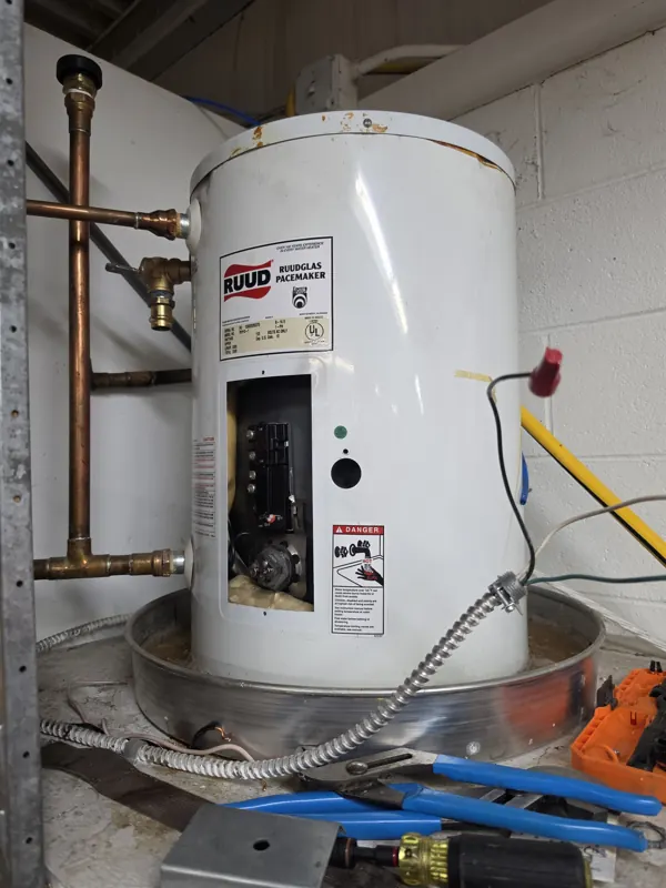 A small point-of-use electric water heater under a counter with corroded fittings