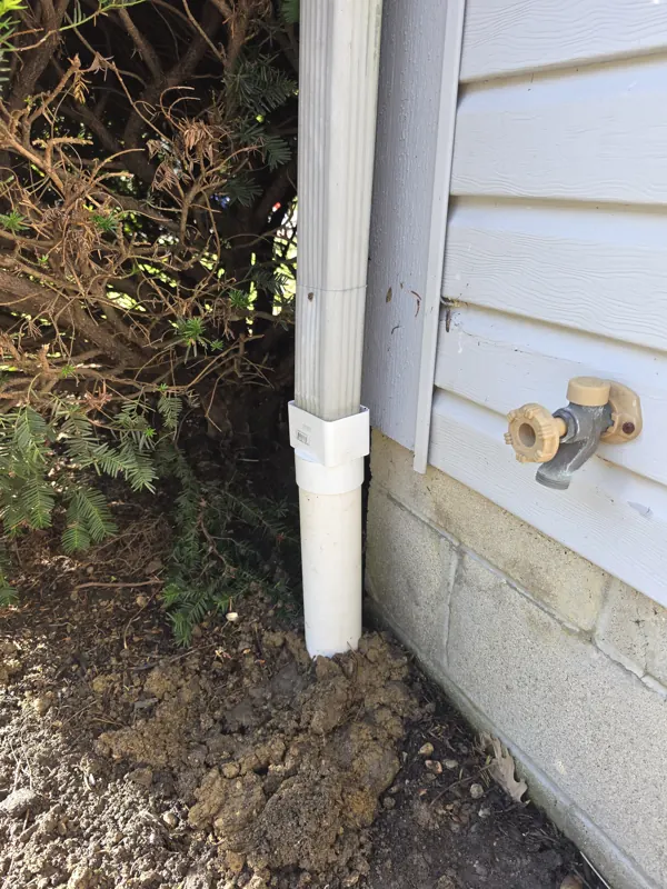 A new PVC downspout adapter and drain connection at a house corner
