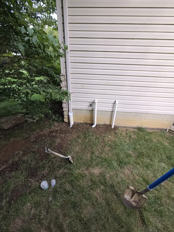 Downspout stubs at the base of a house with the yard opened up beside them