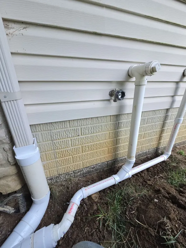 New white PVC downspout connections run along a house foundation