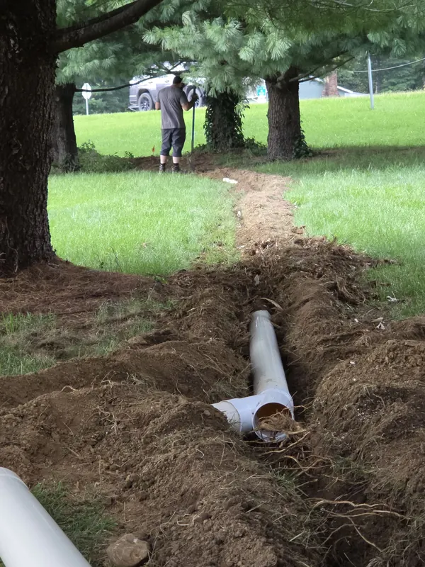 An open trench across a lawn with new PVC drain pipe laid in it