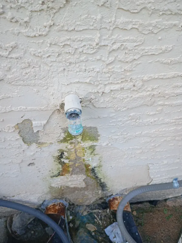 A leaking exterior hose bib on a stucco wall with mineral staining below it