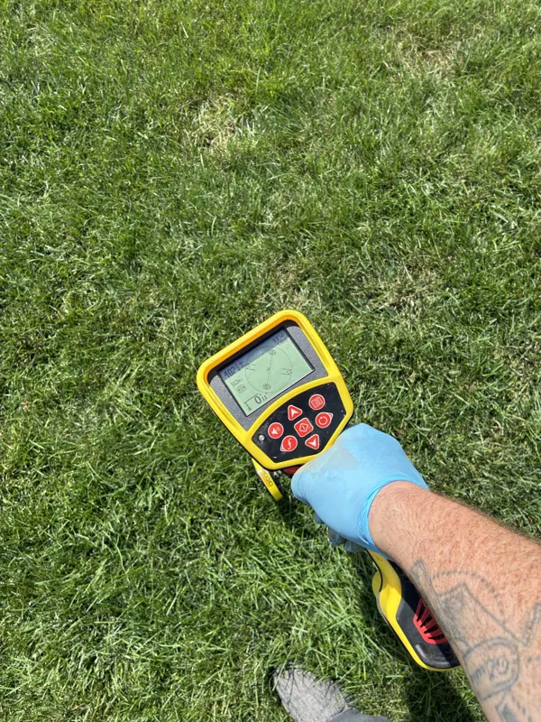 A hand holding a pipe locator over a lawn to find a buried drain line