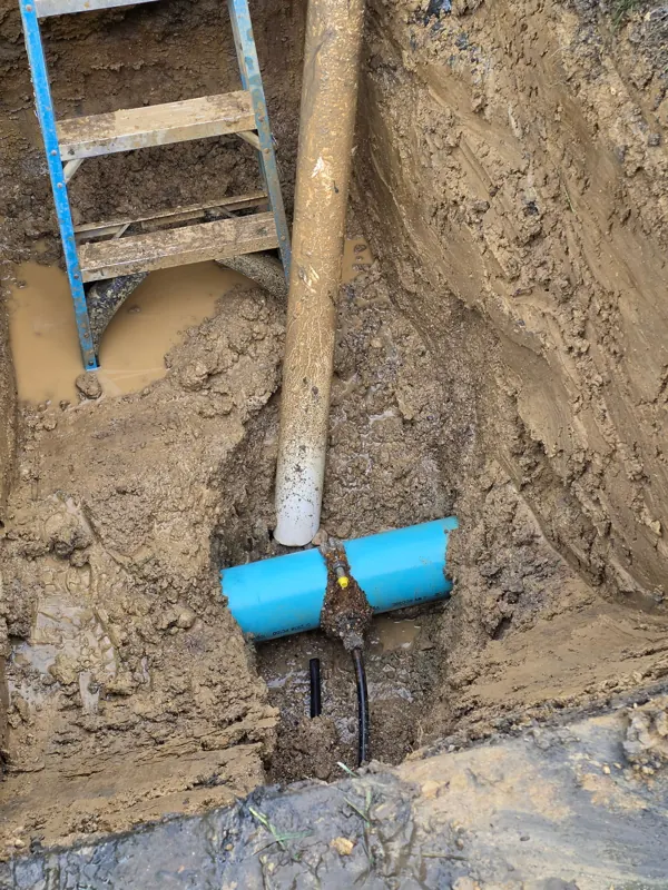 An excavated hole exposing a cracked blue water service pipe and a failed fitting