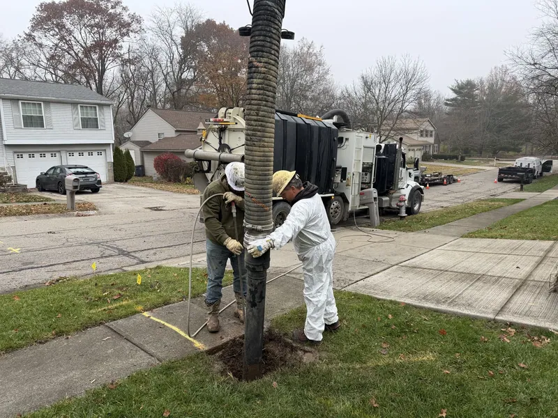 Two crew members working beside a vacuum excavation truck on a residential street