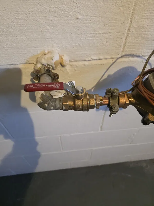 A close view of a brass shut-off valve and fittings on a painted basement wall