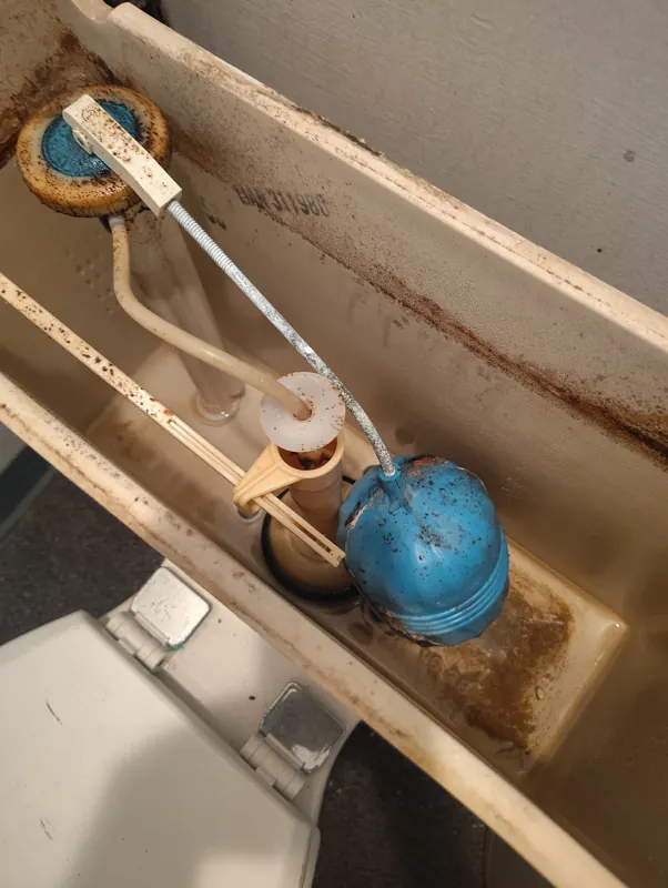 A stained toilet tank interior with a corroded fill valve