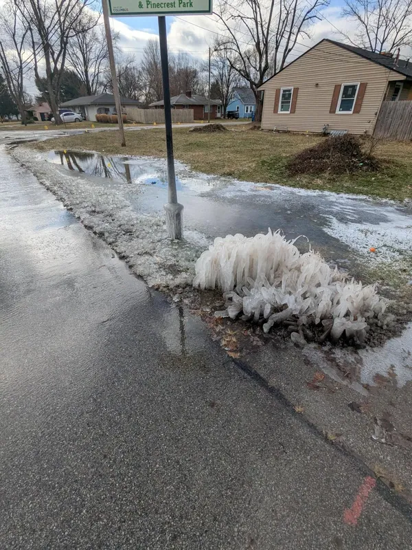 Water from a broken main flowing along a kerb past a house in winter