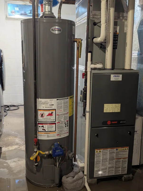 An aging gas water heater beside a furnace in a basement mechanical area